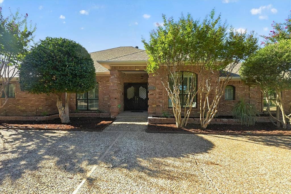Brick exterior, gabled roofline, double entry doors, arched windows, and a gravel driveway