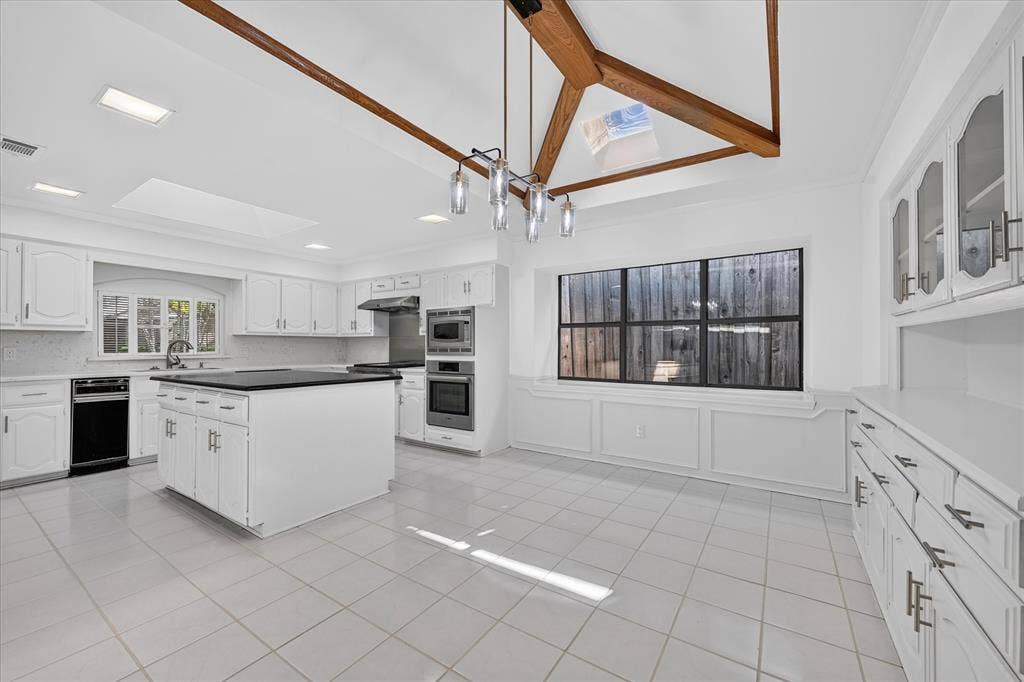 Vaulted ceiling with exposed wood beams, white cabinetry, dark countertops, built-in appliances, and tile flooring
