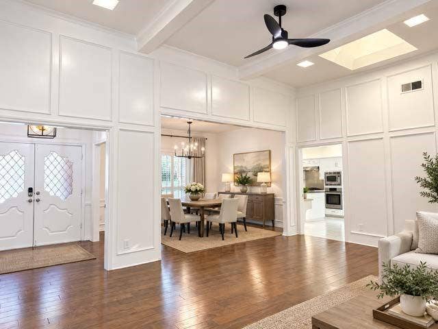 staged Hardwood flooring, decorative wall paneling, ceiling fan with integrated lighting, skylight, and recessed lighting