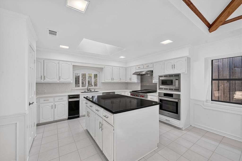 Bright kitchen featuring white cabinetry, a central island with a dark countertop, stainless steel appliances, and tile flooring