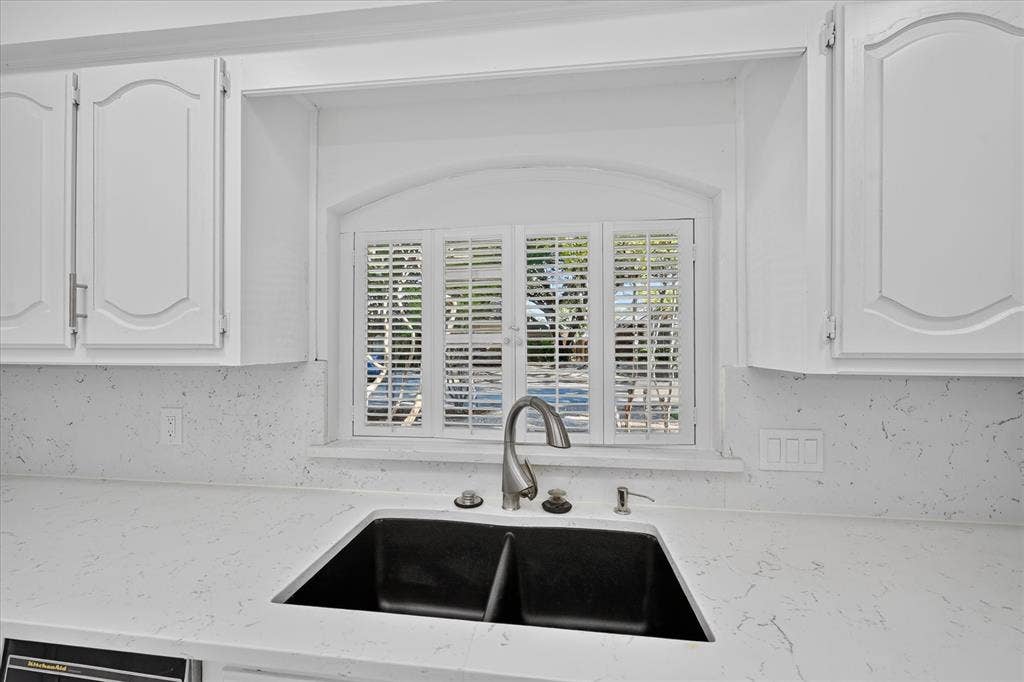 White cabinetry with decorative arch panels, light-toned countertops, and a black undermount double sink with a gooseneck faucet