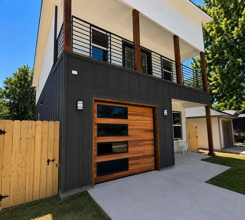 2542 Hooper Street, Dallas, TX 75215 Modern exterior featuring a wood-panel garage door with rectangular windows, dark vertical siding, a second-story balcony with horizontal railings, and a concrete driveway