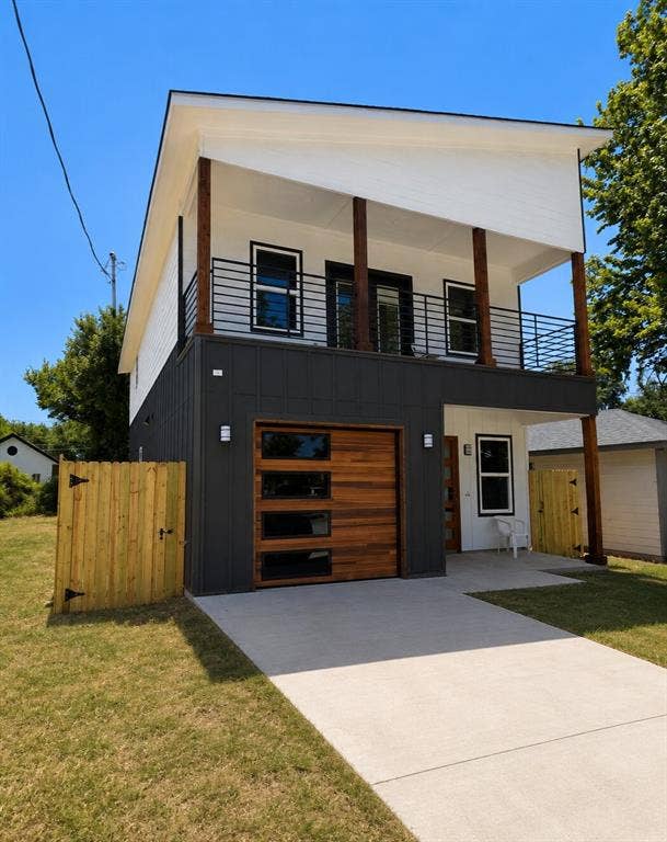 2542 Hooper Street, Dallas, TX 75215 Modern exterior with contrasting dark and white siding, wood garage door with frosted glass panels, upper-level balcony with horizontal bar railing, wood columns, and clear concrete driveway