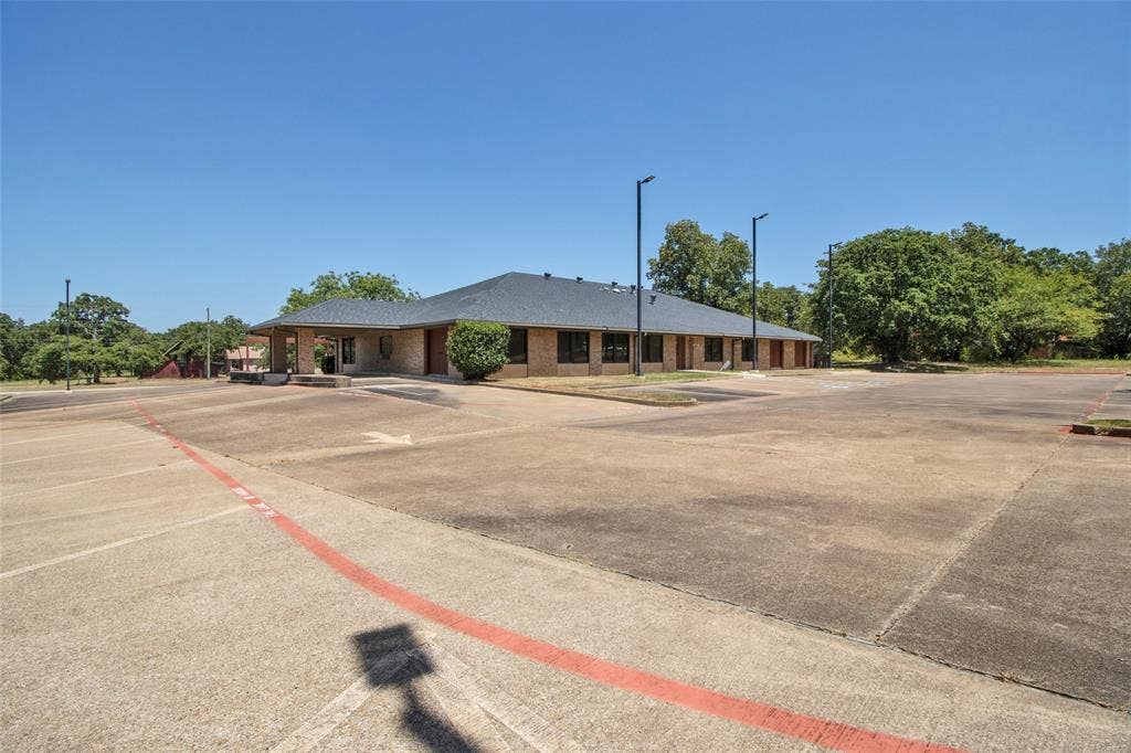 3210 W Northwest Loop 323, Tyler, TX 75702 Expansive concrete parking lot with a brick exterior building and dark roof