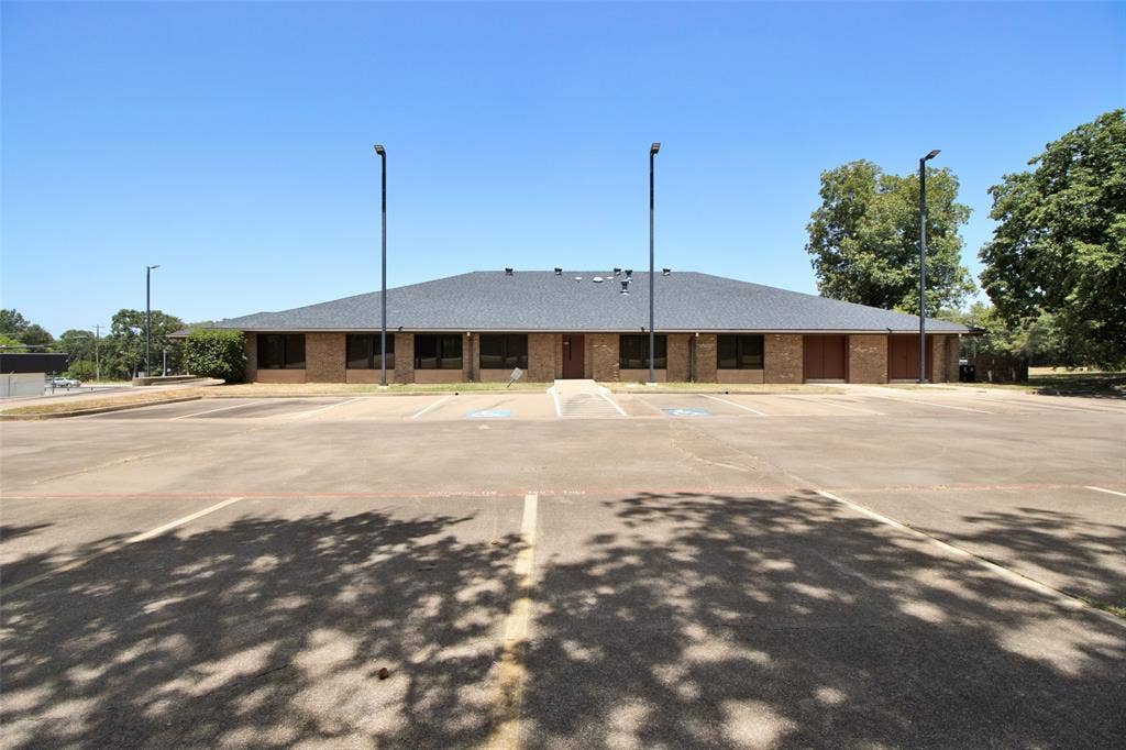 3210 W Northwest Loop 323, Tyler, TX 75702 Brick exterior with a dark shingle roof, expansive paved parking lot, and multiple exterior lighting fixtures