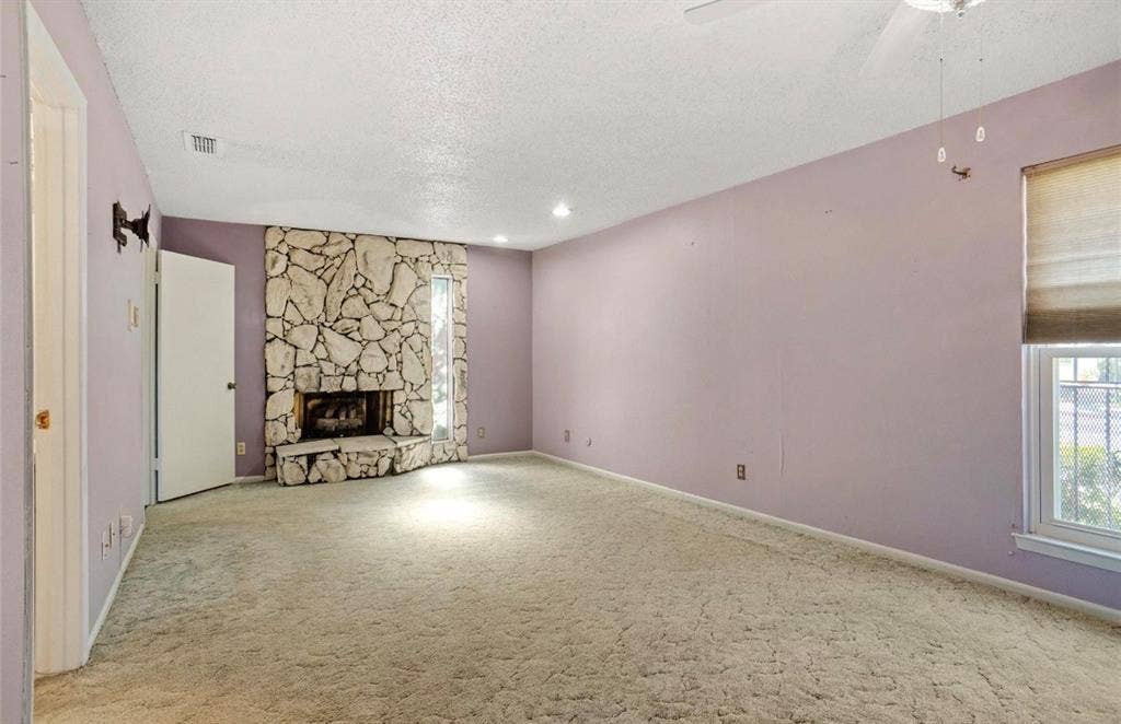 12502 Burninglog Lane, Dallas, TX 75243 Stone-clad fireplace with hearth, recessed lighting, ceiling fan, and window with blinds