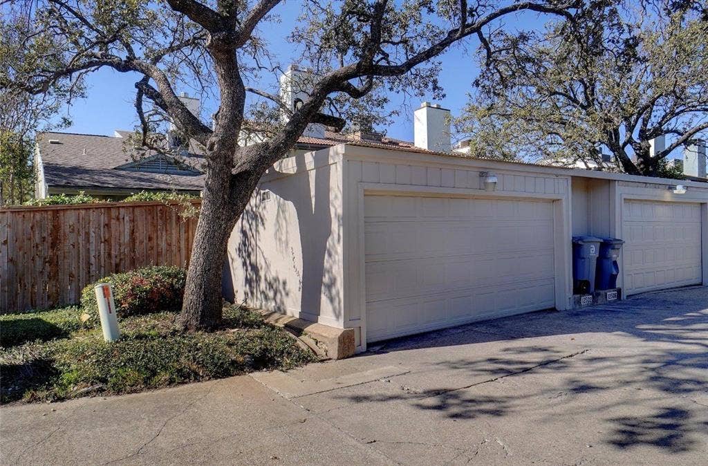 12502 Burninglog Lane, Dallas, TX 75243 Garage with light-colored door, exterior wall-mounted lighting, and a wood privacy fence
