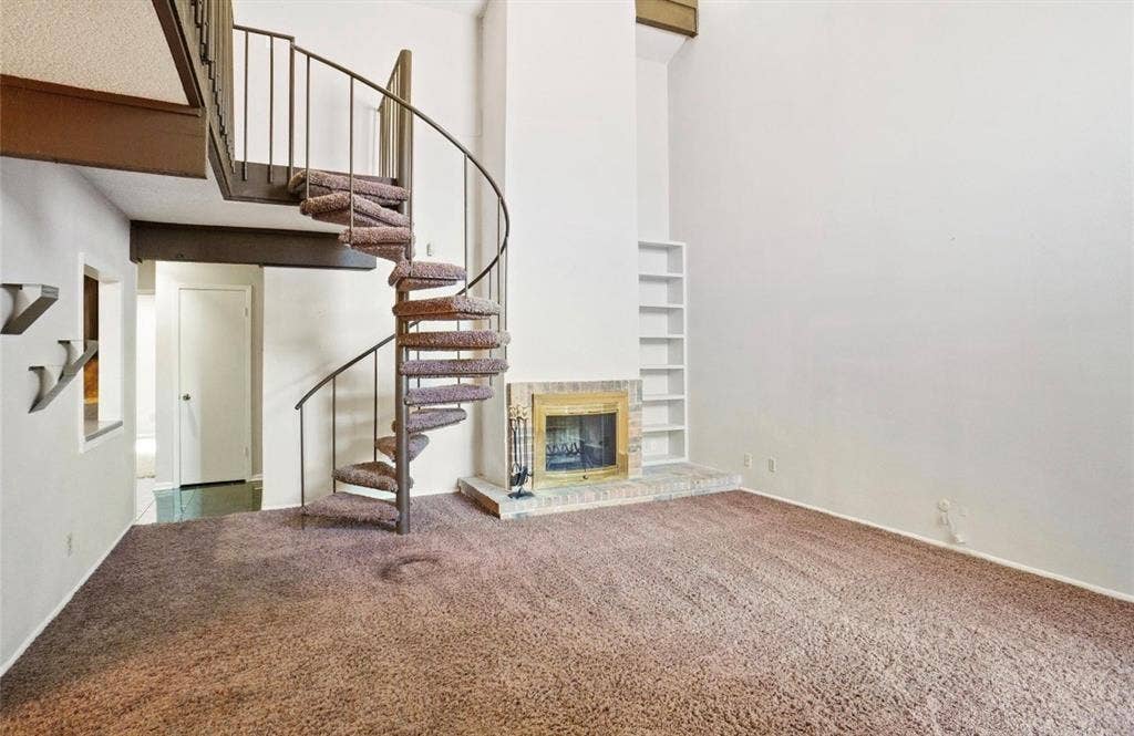 12502 Burninglog Lane, Dallas, TX 75243 Spacious open floor plan featuring neutral carpet flooring, soaring two-story ceilings, and an architectural spiral staircase with metal railings