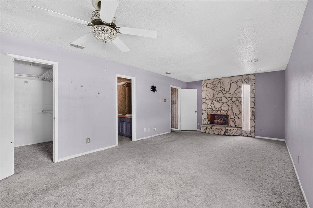 12502 Burninglog Lane, Dallas, TX 75243 Stone-faced fireplace with a hearth, interior closet with shelving, and a ceiling fan with decorative light fixture
