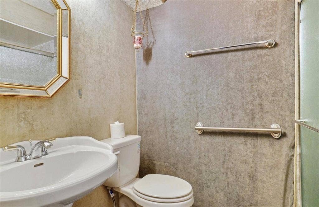 12502 Burninglog Lane, Dallas, TX 75243 Bathroom 2 Pedestal sink with chrome faucet, wall-mounted mirror, toilet, and two grab bars
