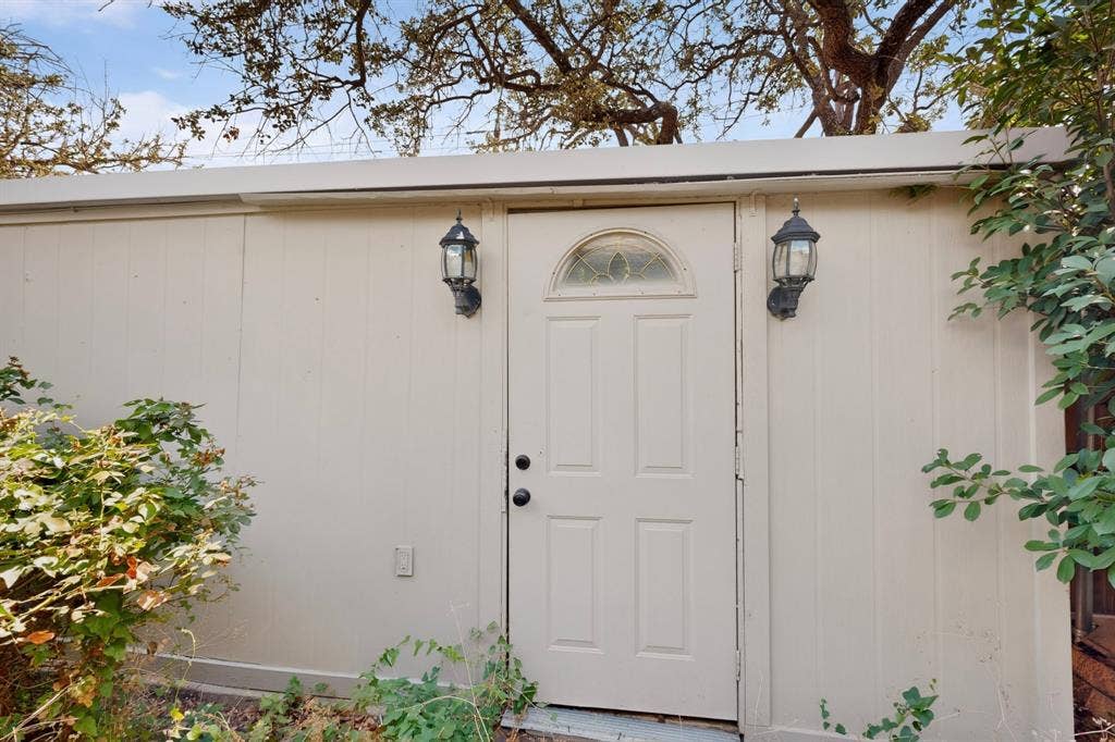 12502 Burninglog Lane, Dallas, TX 75243 Exterior door to detached garage with an arched decorative glass insert and two outdoor sconce lights