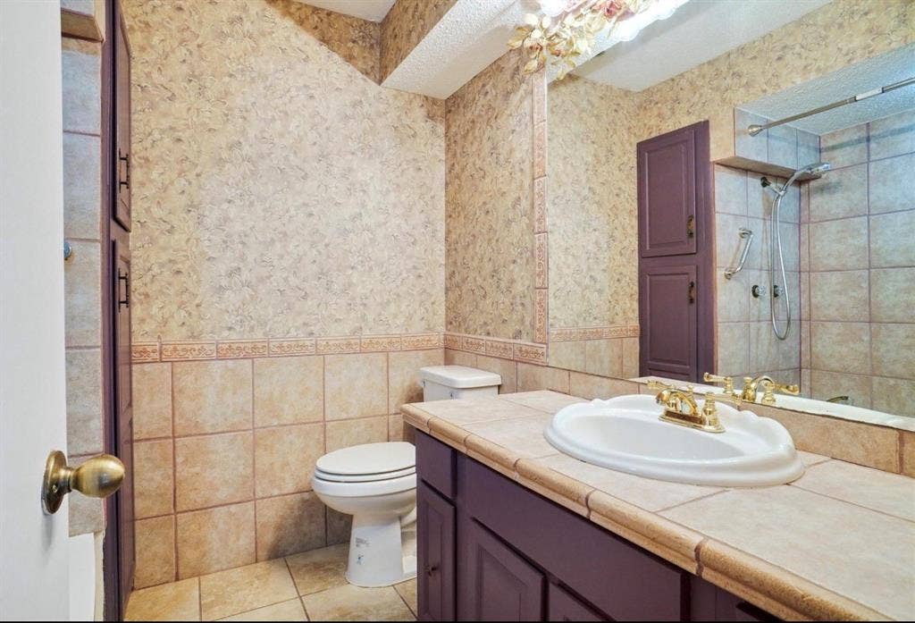 12502 Burninglog Lane, Dallas, TX 75243 Vanity with an integrated sink and brass-finish faucet, tile countertop, built-in cabinetry, and tile flooring