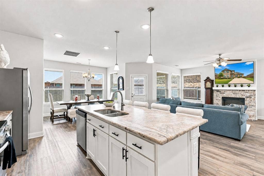 401 Llano Lane, Red Oak, TX 75154 Kitchen island with dual sinks and pendant lighting, wood-finish flooring, recessed lighting, white cabinetry, and a brick fireplace