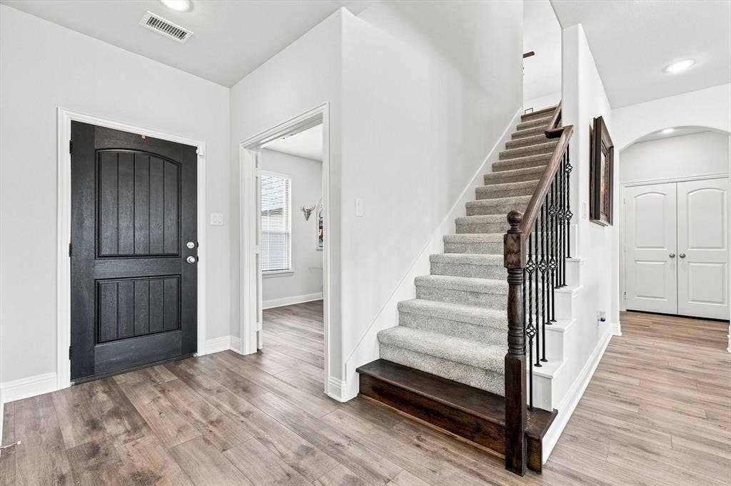 401 Llano Lane, Red Oak, TX 75154 Entryway featuring wood-finish flooring, a dark wood-paneled door, and a staircase with a carpeted runner and wrought iron balusters