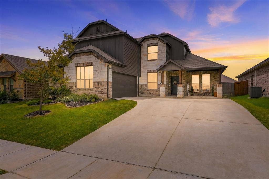 401 Llano Lane, Red Oak, TX 75154 Two-story residence featuring a mixed material facade with brick and stone accents, a concrete driveway, a covered front porch, and an attached garage