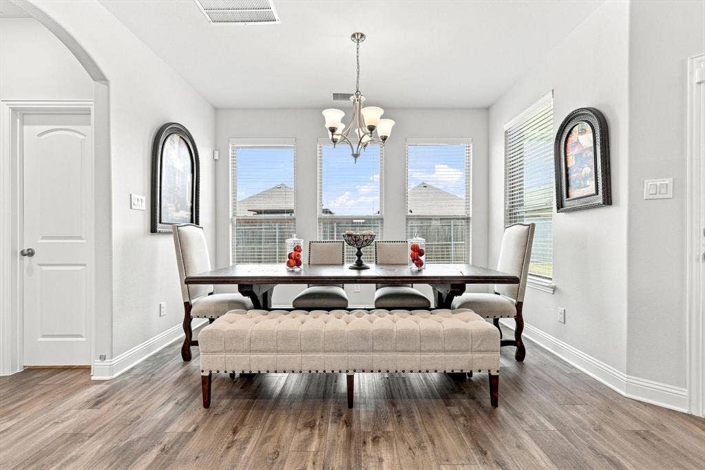 401 Llano Lane, Red Oak, TX 75154 Wood-finish flooring, white trim, arched doorway, three large windows, and a chandelier with glass shades