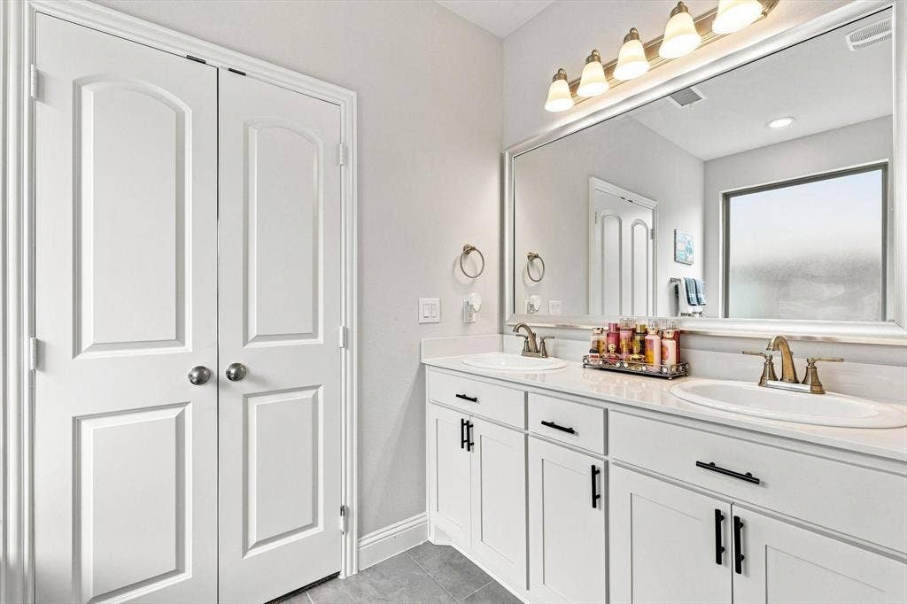 401 Llano Lane, Red Oak, TX 75154 Dual white vanities with integrated sinks, brass-finish faucets, expansive framed mirror, and a multi-bulb vanity light fixture