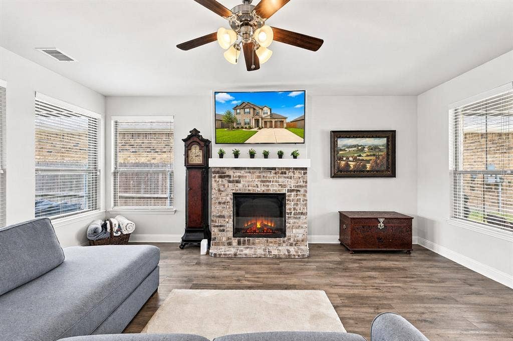 401 Llano Lane, Red Oak, TX 75154 Living space featuring wood-finish flooring, a brick-surround fireplace with a mantel, multiple windows with blinds, and a ceiling fan