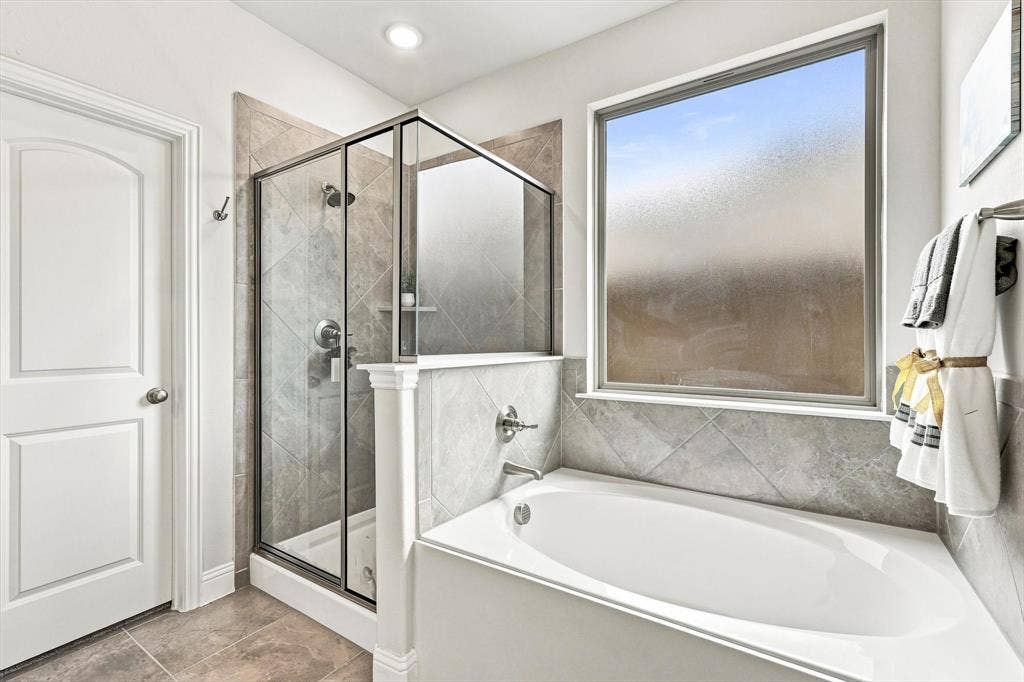 401 Llano Lane, Red Oak, TX 75154 White paneled door, glass-enclosed shower with tiled walls, built-in bathtub, and a large window with privacy glass