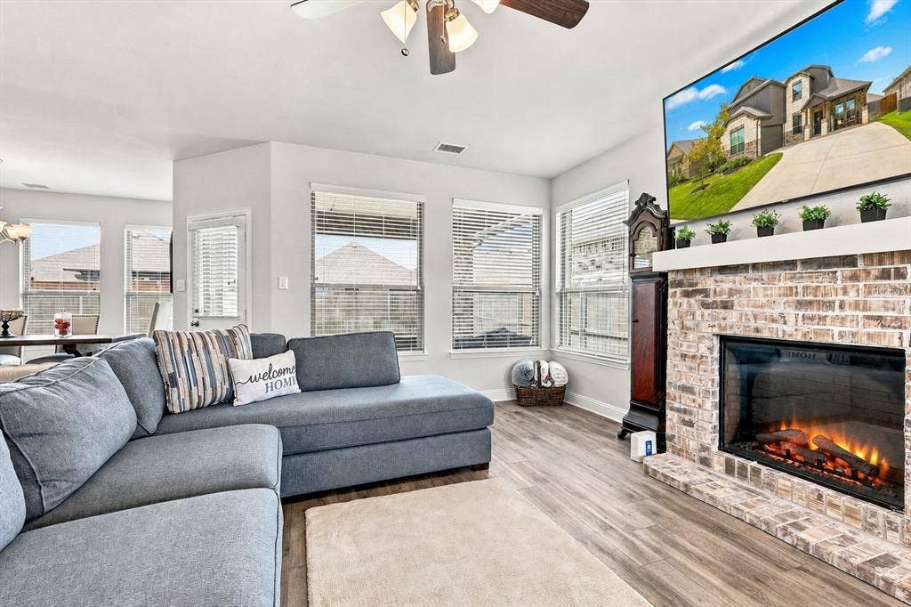 401 Llano Lane, Red Oak, TX 75154 Spacious living area featuring wood-finish flooring, a brick-surround fireplace, and multiple windows with blinds