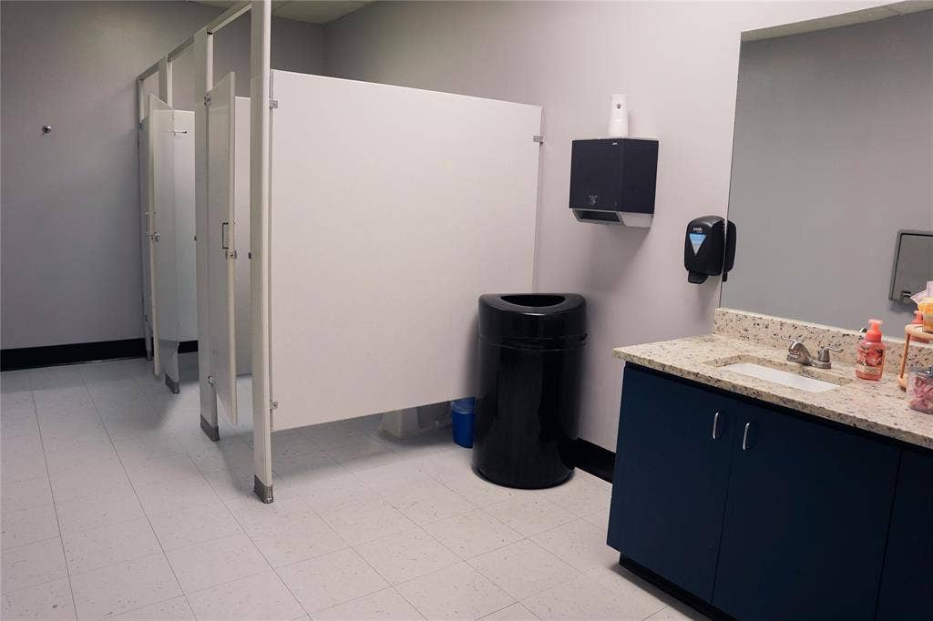 2705 Virginia Parkway, #SLE, McKinney, TX 75071 Restroom featuring multiple stalls with privacy panels, a vanity with a light-colored countertop, an integrated sink basin, and a wall-mounted mirror