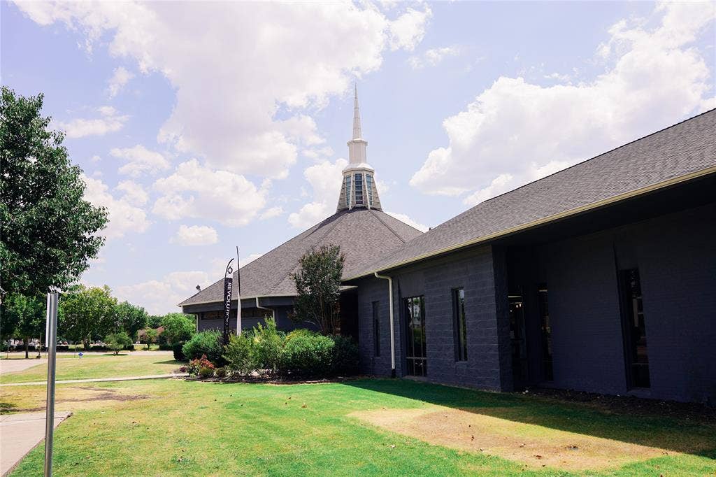 2705 Virginia Parkway, #SLE, McKinney, TX 75071 Pitched shingle roof with a prominent white steeple, exterior walls finished in dark gray, and surrounding green landscaping