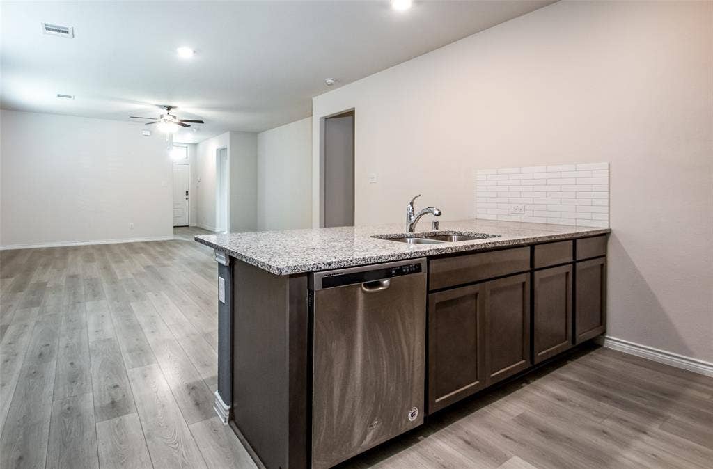 2721 Franklin Drive, Celina, TX 75009 Kitchen island with a stainless steel sink, chrome faucet, stone countertop, and subway tile backsplash