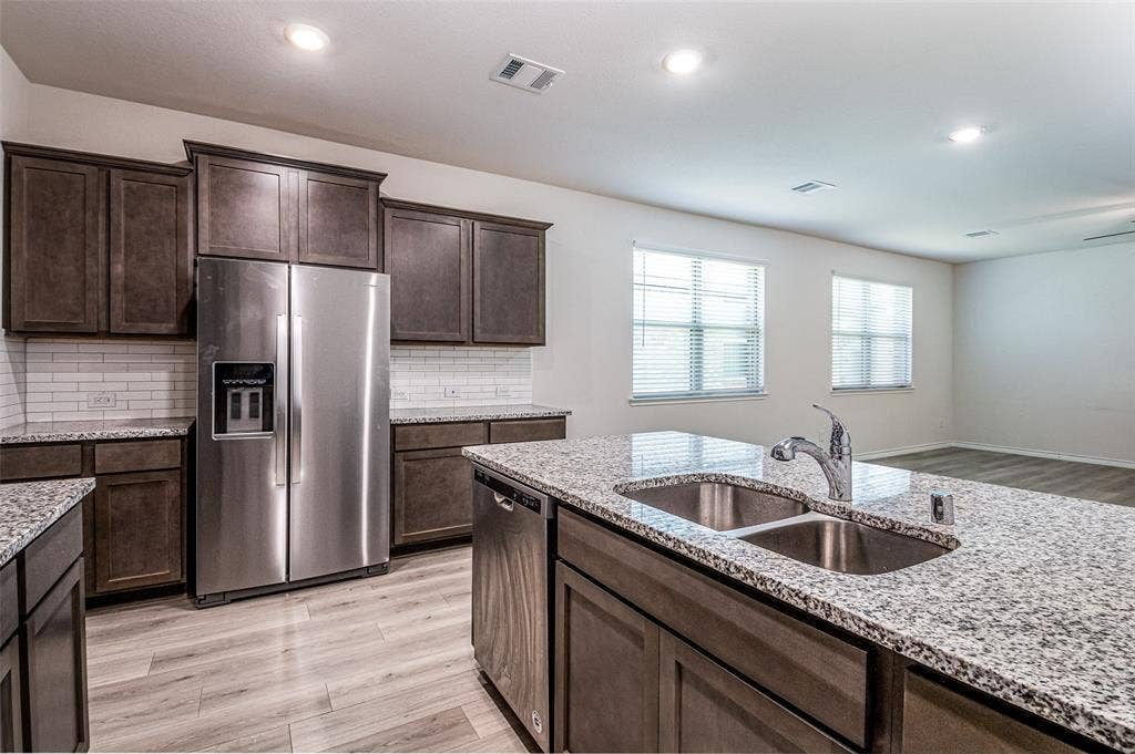 2721 Franklin Drive, Celina, TX 75009 Kitchen featuring dark wood-finish cabinetry, stainless steel appliances, granite countertops, white subway tile backsplash, and wood-finish flooring