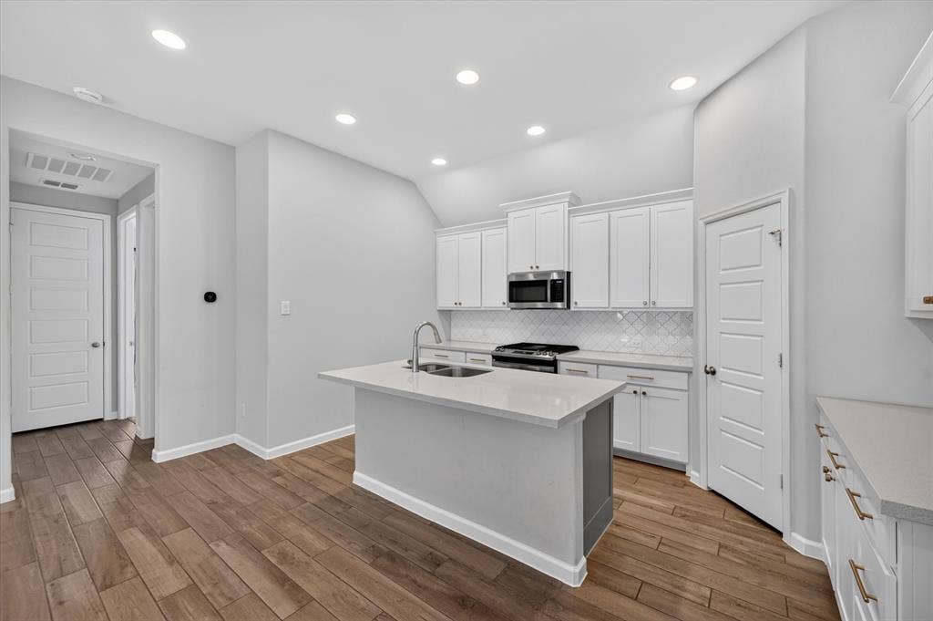 5308 Tupper Avenue, Fate, TX 75087 Modern kitchen featuring white cabinetry, stainless steel appliances, a white tile backsplash, a central island with a sink, and wood-finish flooring