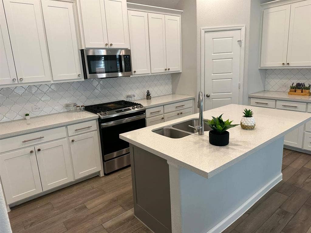 5308 Tupper Avenue, Fate, TX 75087 Kitchen featuring white shaker cabinetry, stainless steel appliances, patterned tile backsplash, light-toned countertops, and wood-finish flooring