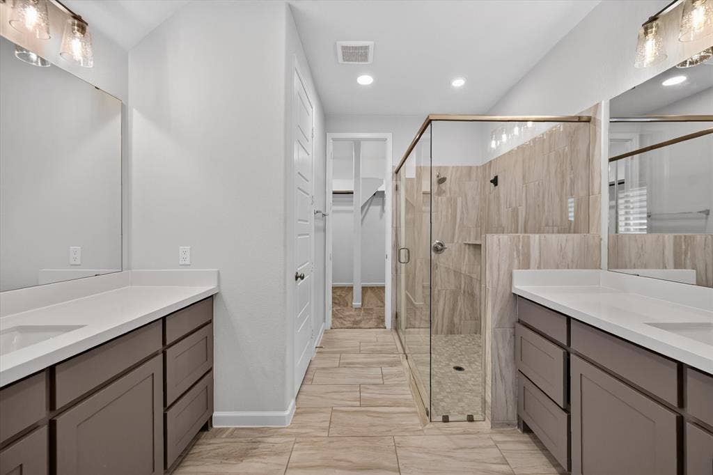 5308 Tupper Avenue, Fate, TX 75087 Dual vanities with white countertops, a frameless glass shower enclosure, wood-finish flooring, and recessed lighting
