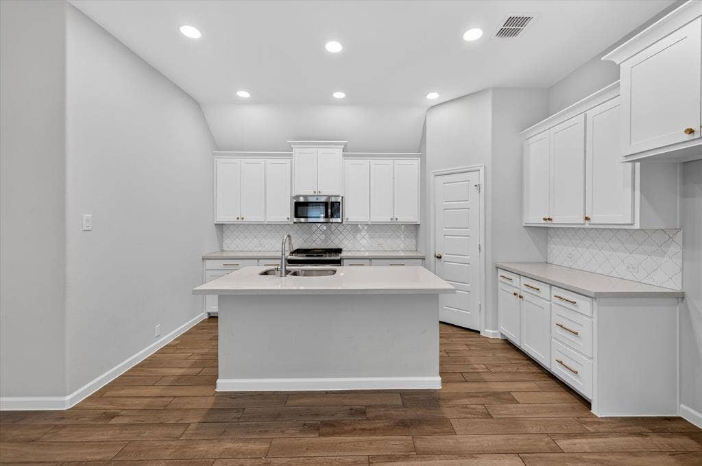 5308 Tupper Avenue, Fate, TX 75087 Kitchen featuring an island with an undermount sink, white cabinetry, stainless steel microwave, and wood-finish flooring