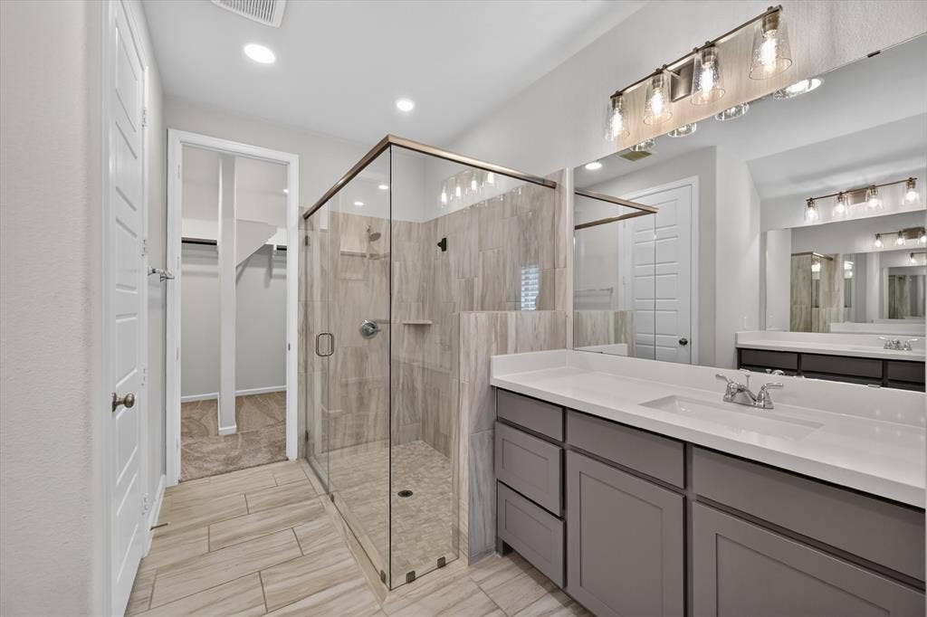 5308 Tupper Avenue, Fate, TX 75087 Glass-enclosed shower with tile surround and floor, dual vanity with undermount sinks and white countertops, tile flooring, and overhead vanity lighting