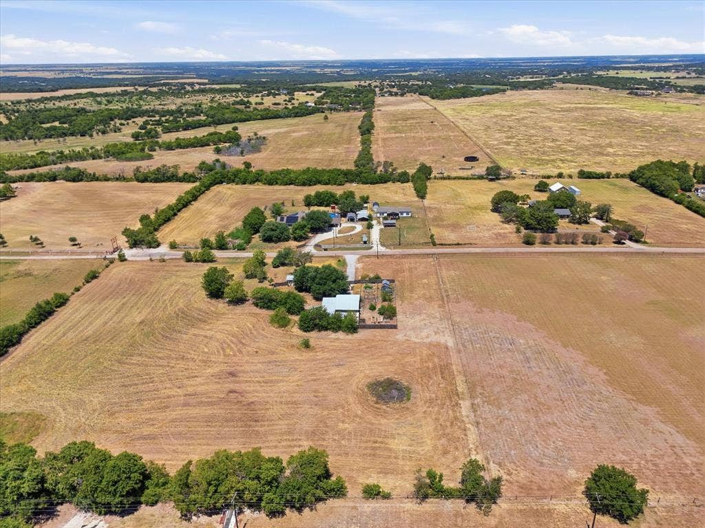 TBD Lot 1 Bluebonnett Lane, Lorena, TX 76655 Expansive agricultural land with a distant rural landscape, featuring multiple buildings and scattered mature trees