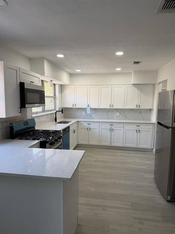 806 S Atkerson Lane, Euless, TX 76040 Full kitchen featuring white shaker cabinetry, stainless steel appliances, light-toned wood-finish flooring, recessed lighting, and light-toned countertops with matching backsplash