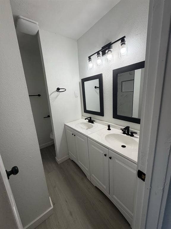 806 S Atkerson Lane, Euless, TX 76040 Dual vanity with integrated sinks, white cabinetry, dark-framed mirrors, matte black hardware, and wood-finish flooring