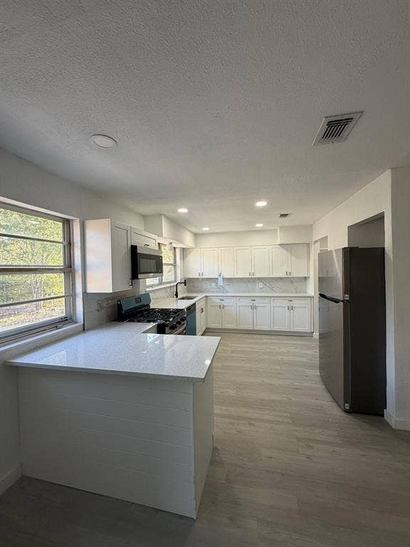 806 S Atkerson Lane, Euless, TX 76040 Kitchen featuring white cabinetry, light-toned countertops, a full suite of stainless steel appliances, and wood-finish flooring