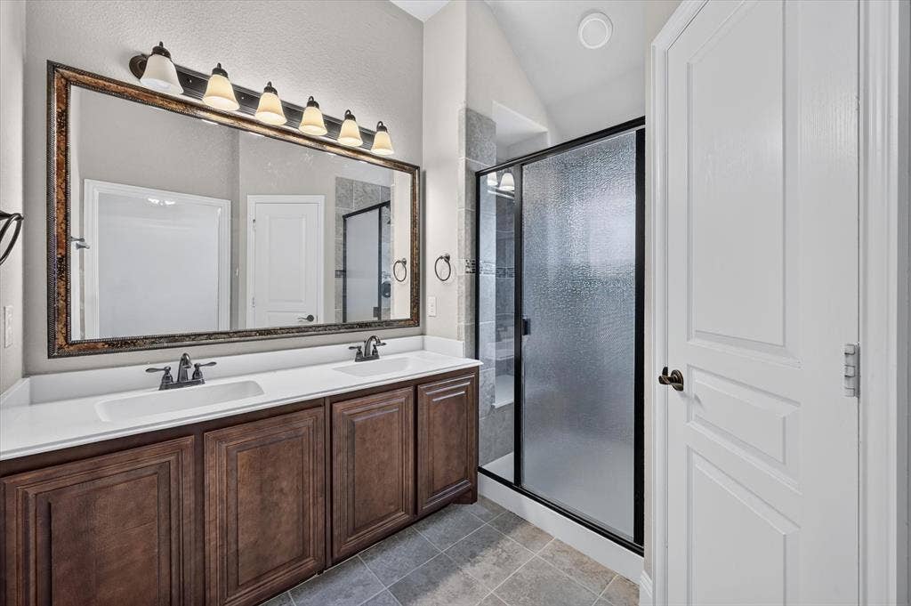 316 Jernigan Drive, Euless, TX 76040 Upstairs Primary Bathroom 2 Dual vanity with integrated sinks, framed mirror, six-light fixture, tiled flooring, and a glass-enclosed shower