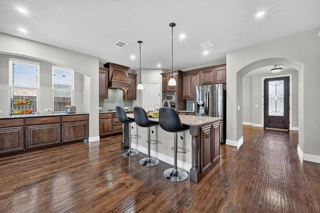 316 Jernigan Drive, Euless, TX 76040 Spacious kitchen featuring rich wood cabinetry, stone countertops, a large island with seating, stainless steel appliances, and wood-finish flooring