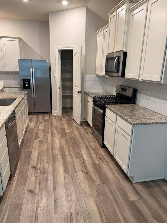 1001 Calhoun Drive, Anna, TX 75409 Kitchen with wood-finish flooring, white cabinetry, integrated stainless steel appliances, speckled countertops, and a subway tile backsplash