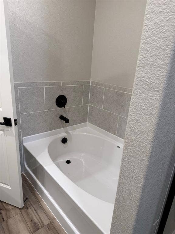 1001 Calhoun Drive, Anna, TX 75409 White bathtub with matte black fixtures, grey tiled surround, and wood-finish flooring