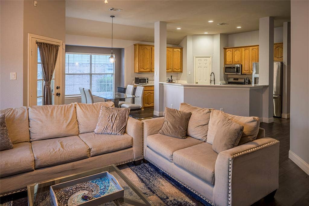Open-concept living area featuring dark wood-finish flooring, recessed lighting, and a kitchen with wood cabinetry and stainless steel appliances