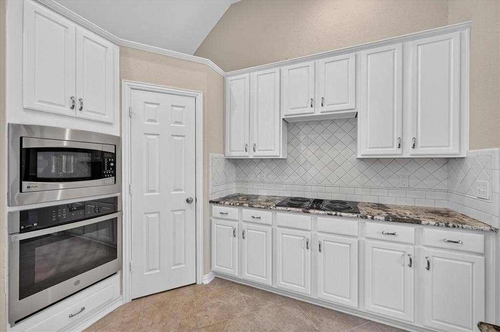 10307 Perkins Drive, Irving, TX 75063 White cabinetry, built-in stainless steel microwave and oven, cooktop, patterned tile backsplash, and stone-finish countertops