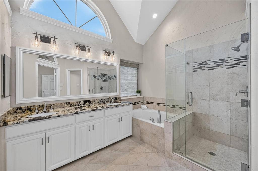 10307 Perkins Drive, Irving, TX 75063 Spa-inspired primary bathroom featuring a triple-vanity with granite countertop and polished nickel hardware, a freestanding soaking tub, and a walk-in shower with glass enclosure and linear tile detailing