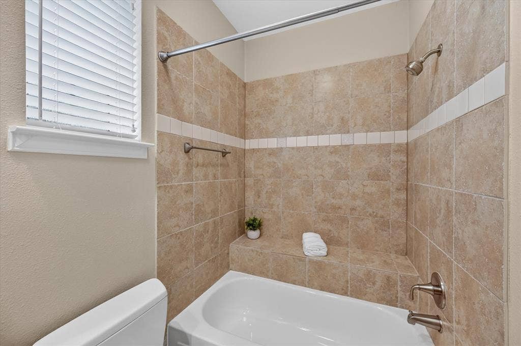 10307 Perkins Drive, Irving, TX 75063 Tub and shower combination featuring floor-to-ceiling tile surround, an integrated tiled bench, and brushed nickel fixtures