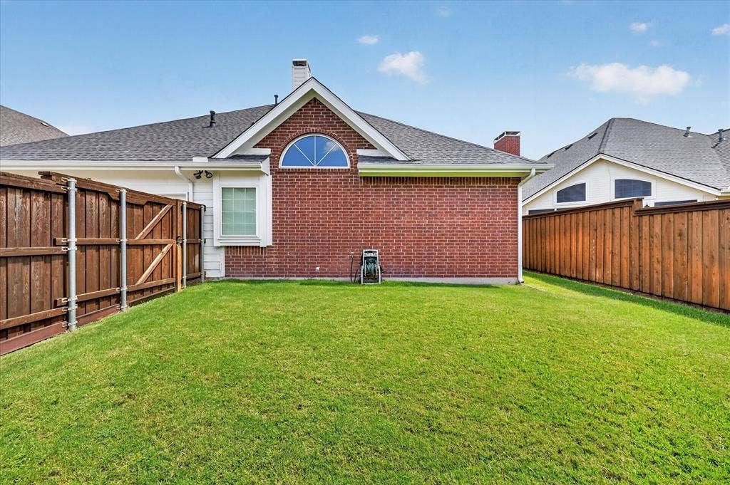 10307 Perkins Drive, Irving, TX 75063 Expansive green lawn with a wood plank privacy fence and brick exterior