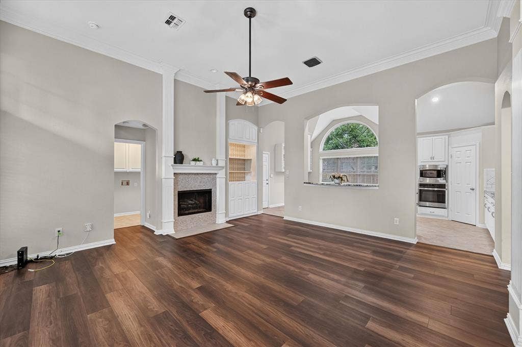 10307 Perkins Drive, Irving, TX 75063 Wood-finish flooring, recessed fireplace with tile surround, built-in shelving, arched doorways, and crown molding