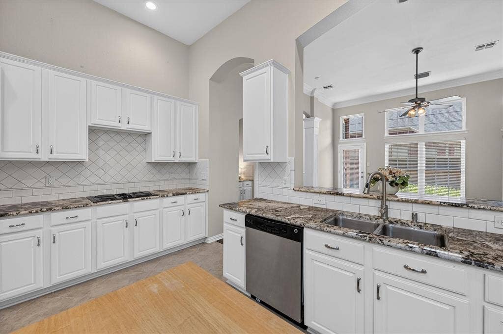 10307 Perkins Drive, Irving, TX 75063 Kitchen featuring white cabinetry, dark speckled countertops, subway tile backsplash, stainless steel appliances, and a double basin sink