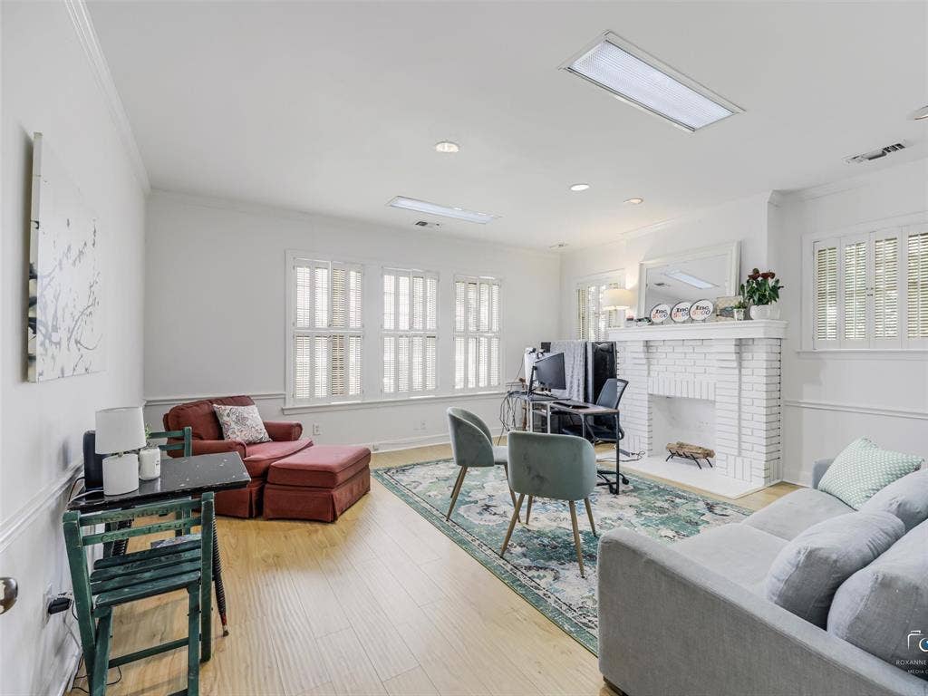 4310 Gaston Avenue, #103, Dallas, TX 75246 Spacious living area featuring wood-finish flooring, white brick fireplace, multiple windows with plantation shutters, and recessed lighting