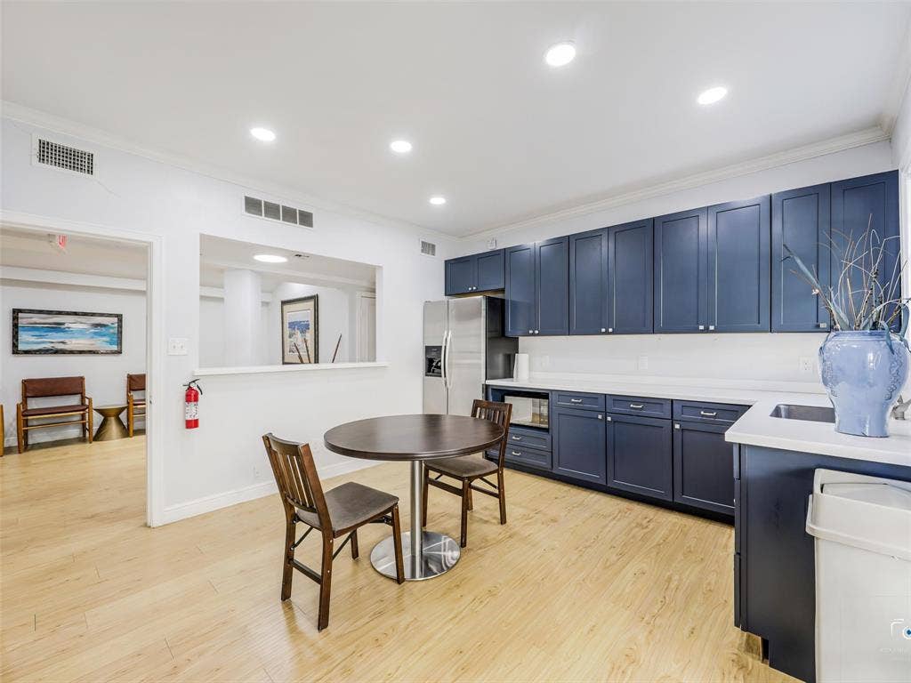 4310 Gaston Avenue, #103, Dallas, TX 75246 Modern kitchen and dining area featuring custom navy cabinetry with polished hardware, white quartz countertops, stainless steel appliances, wood-finish flooring throughout, and recessed ceiling lighting
